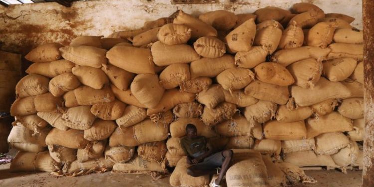 A worker sits near a pile of sacks of cocoa at a warehouse in Soubre, Ivory Coast January 8, 2021. Picture taken January 8, 2021. REUTERS/Luc Gnago