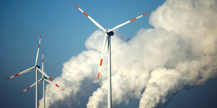 Steam billows from coal power station behind wind turbines