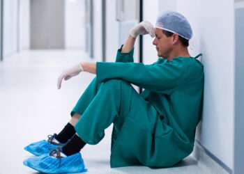 Tensed male surgeon sitting in corridor of hospital
