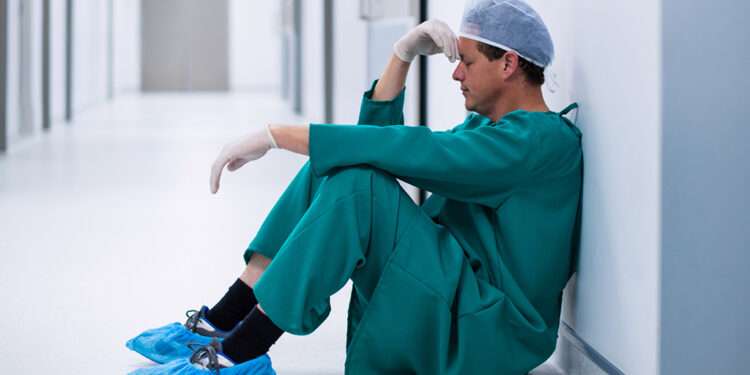 Tensed male surgeon sitting in corridor of hospital