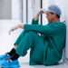 Tensed male surgeon sitting in corridor of hospital