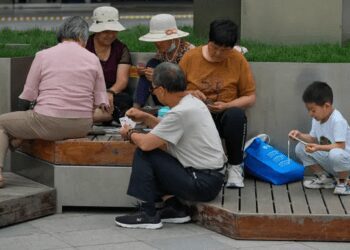 Adults play cards on a bench as a child plays with a smartphone.