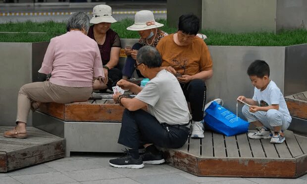 Adults play cards on a bench as a child plays with a smartphone.