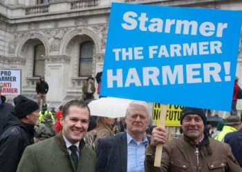 Robert Jenrick poses under a ‘Starmer the farmer harmer’ banner