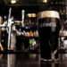 Zoom in on a glass with cold dark Guinness beer with a thin strip of completely settled foam in a Bar. High quality 4k footage