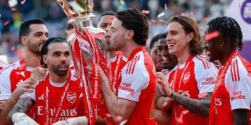 Declan Rice kisses the Premier League trophy while celebrating with his Arsenal teammates at Selhurt Park