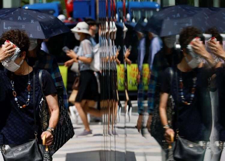 Japan Swelters in Worst Heatwave Since 1875 1 A woman wipes her face as she walks down a street in Tokyo