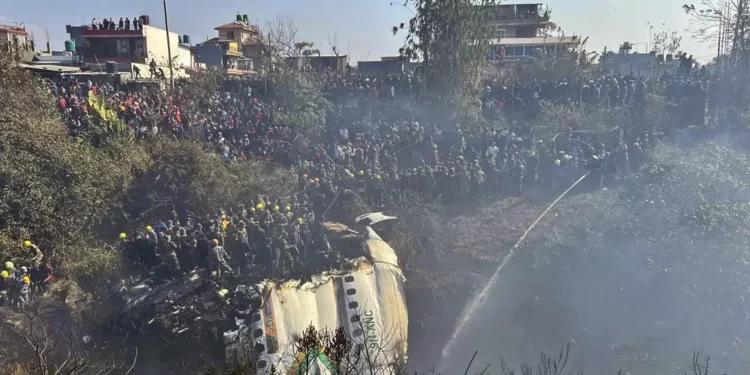 Locals watch the wreckage of a passenger plane as rescuers search the crash site, in Pokhara, Nepal.