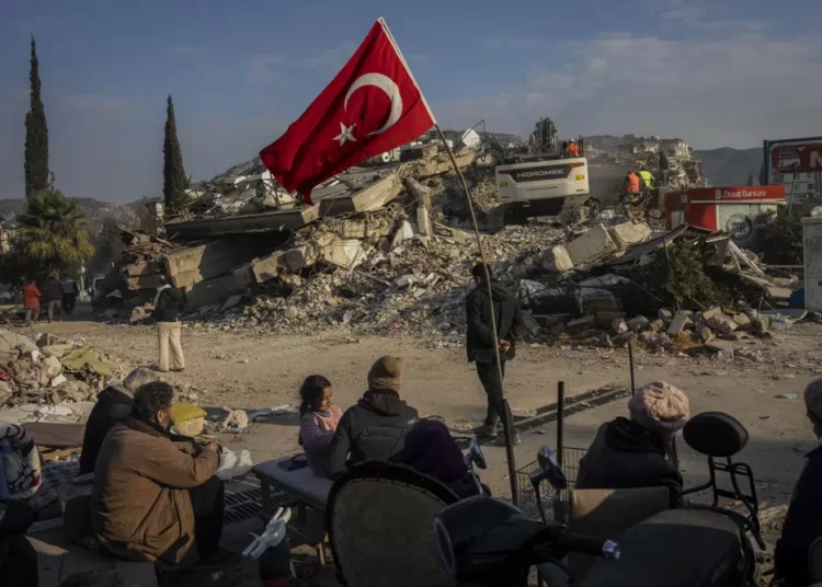 A family sit next to a collapsed building as they wait for the bodies of their relatives to be recovered from under the rubble in Antakya, southeastern Turkey