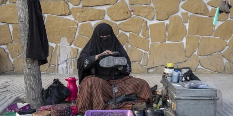 An Afghan woman cleans customers's shoes in a street in Kabul, Afghanistan