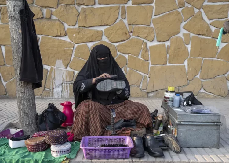 An Afghan woman cleans customers's shoes in a street in Kabul, Afghanistan