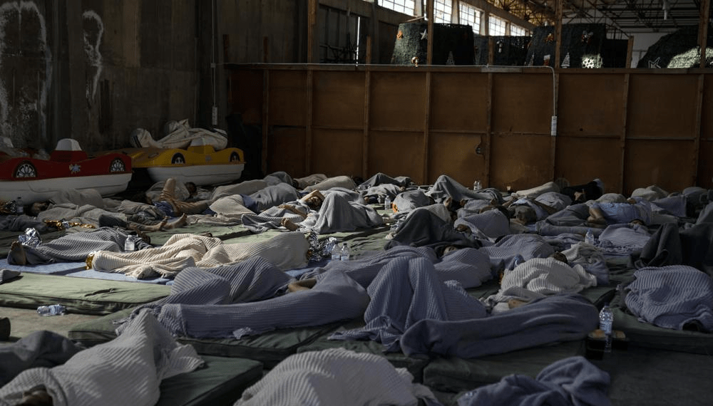 Survivors of a shipwreck sleep at a warehouse at the port in Kalamata town, about 240 kilometers (150 miles) southwest of Athens, Wednesday, June 14, 2023.