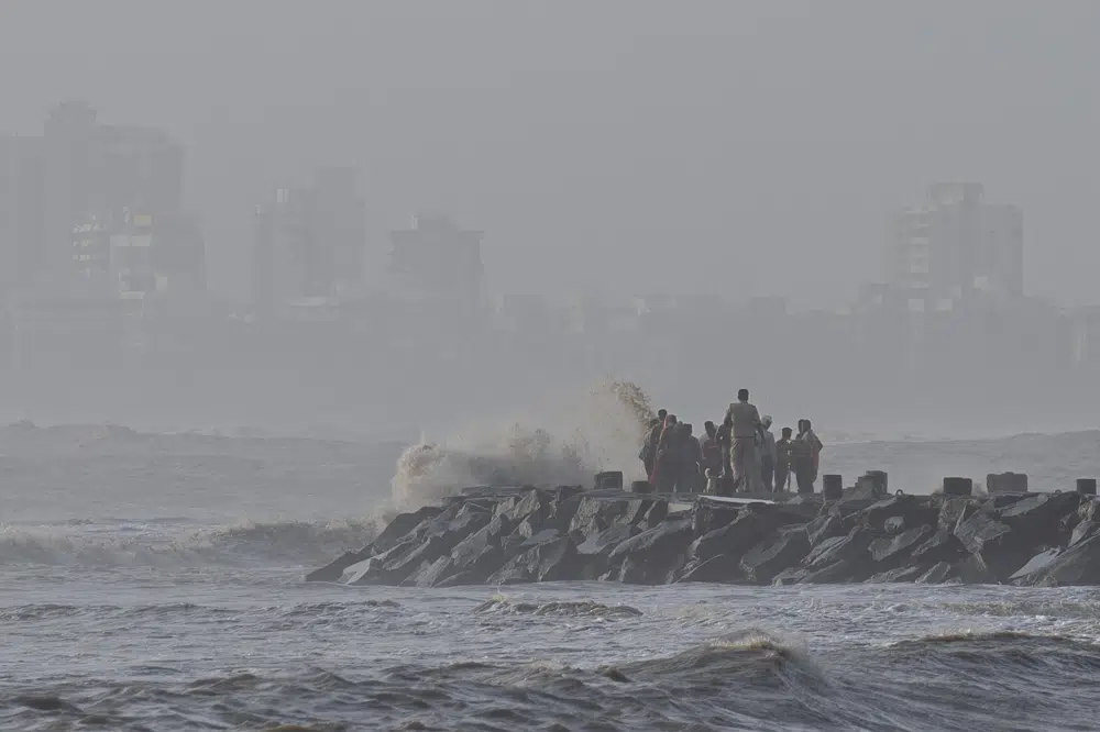 A police officer tries to move people away as high tide waves hit the Arabian Sea coast at Juhu Koliwada