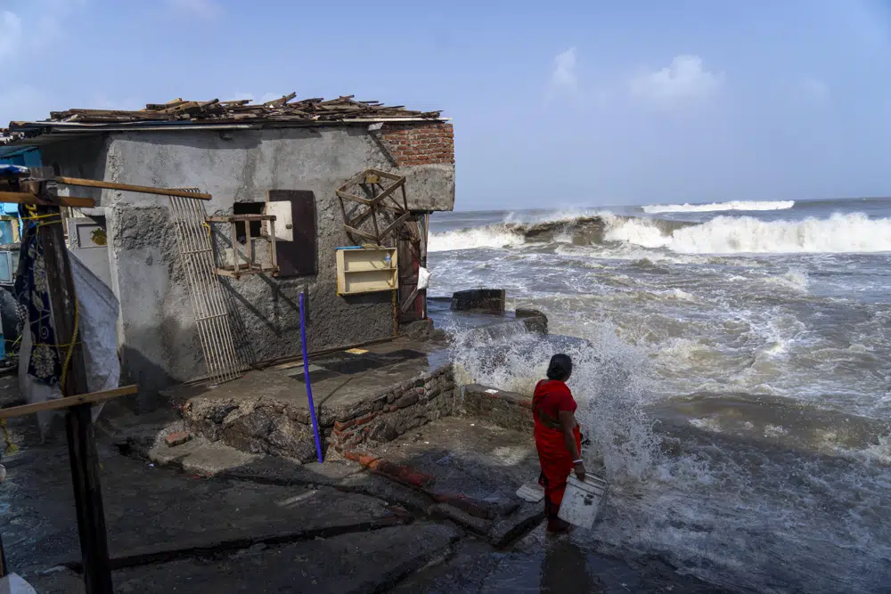 A woman stands next to her house as high tide waves hit the Arabian Sea coast in Mumbai