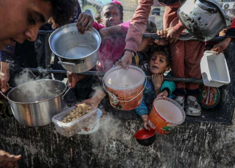 Palestinian children wait in line to receive food prepared by volunteers for Palestinian families displaced to Southern Gaza due to Israeli attacks, between rubble of destroyed buildings in Rafah, Gaza, on February 9, 2024.