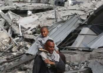 A Palestinian man carries his child on his shoulders as he walks past damaged buildings in Khan Younis on April 8, 2024 after Israel pulled its ground forces out of the southern Gaza Strip.
