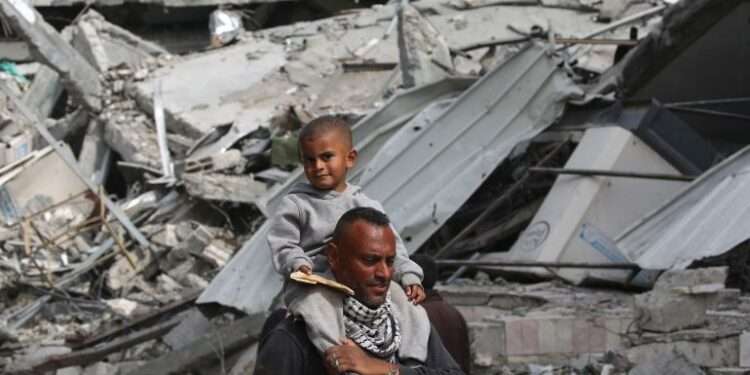 A Palestinian man carries his child on his shoulders as he walks past damaged buildings in Khan Younis on April 8, 2024 after Israel pulled its ground forces out of the southern Gaza Strip.