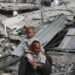 A Palestinian man carries his child on his shoulders as he walks past damaged buildings in Khan Younis on April 8, 2024 after Israel pulled its ground forces out of the southern Gaza Strip.