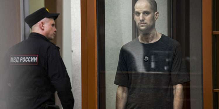 Wall Street Journal reporter, Evan Gershkovich, stands listening to the verdict in a glass cage.