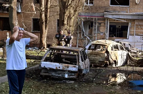 A man reacts while standing next to burnt-out remains of cars in the courtyard of a multi-storey residential building in Kursk, Russia.