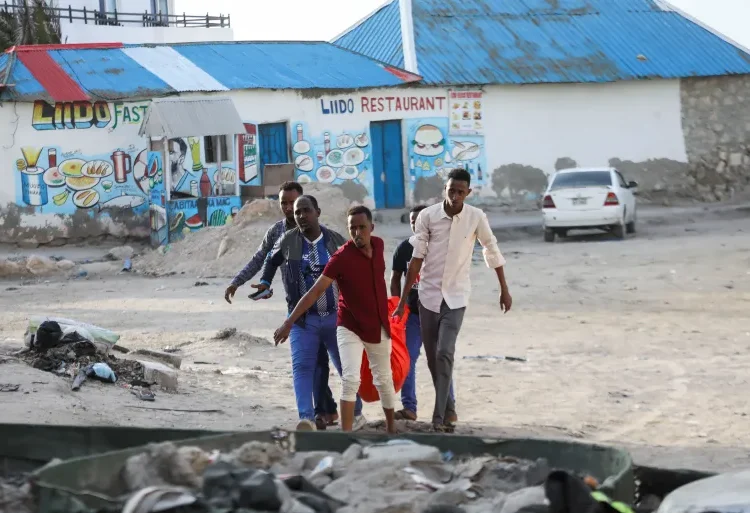 People carry the dead body of an unidentified woman killed in an explosion  at the Lido beach in Mogadishu, Somalia