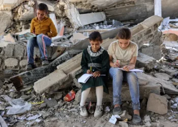 Children write in notebooks sitting on a destroyed building near a tent being used as a makeshift educational centre for primary school students in Jabalia in northern Gaza.