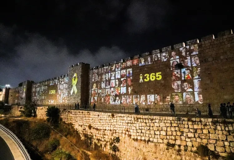 Fate Of Remaining Captives Contingent On Israel’s Actions 1 People walk by the walls of Jerusalem’s Old City as pictures of people taken captive during the October 7 attack on Israel are projected on them.