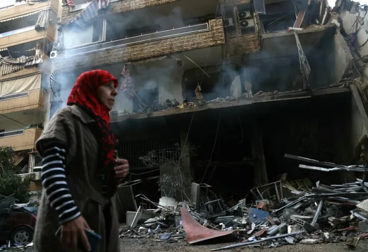 Israel-Hezbollah Ceasefire Takes Effect 1 A woman walks past a building damaged by Israeli airstrikes on Tayouneh in Beirut's suburban outskirts.