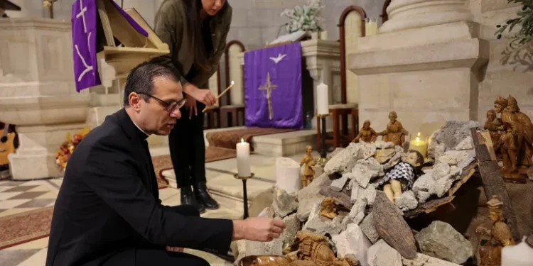 Pastor Munther Isaac adds dirt to an installation that shows a figure symbolizing baby Jesus lying amidst the rubble in a grotto ahead of Christmas at the Evangelical Lutheran Church, in the Israeli-occupied West Bank.