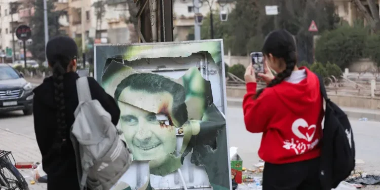 Al-Assad’s Ouster Perceived To Be A Blessing And A Curse 1 Residents of Qamishli in Syria use their mobile phones to capture a damaged picture of Syrian President Bashar al-Assad as people celebrate the ousting of the President.
