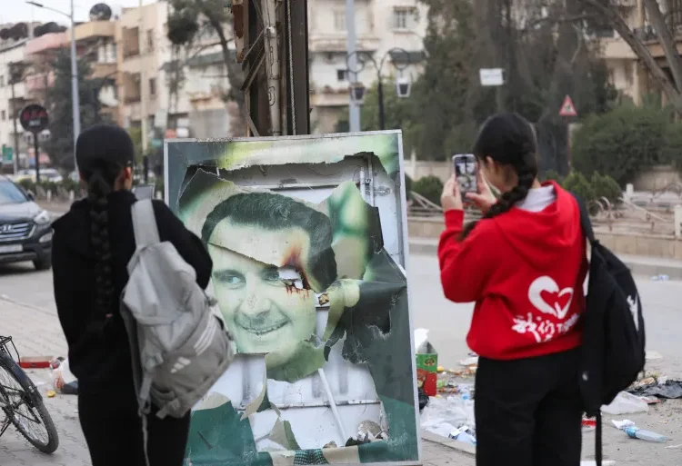 Residents of Qamishli in Syria use their mobile phones to capture a damaged picture of Syrian President Bashar al-Assad as people celebrate the ousting of the President.