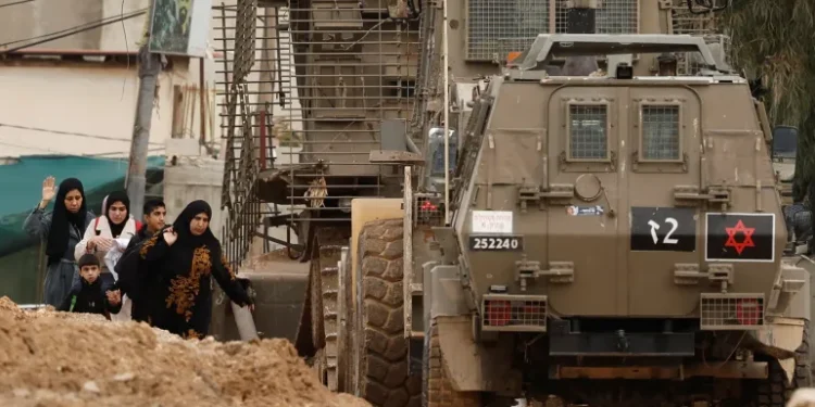 Palestinians women and children, one with arms raised, walk next to Israeli military vehicles on a damaged street as they flee the Jenin refugee camp in the occupied West Bank.