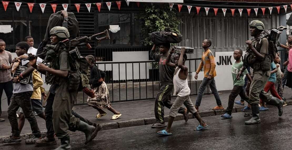 Residents walk alongside members of the M23 armed group in the city of Goma after it was besieged