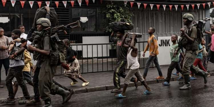 Residents walk alongside members of the M23 armed group in the city of Goma after it was besieged