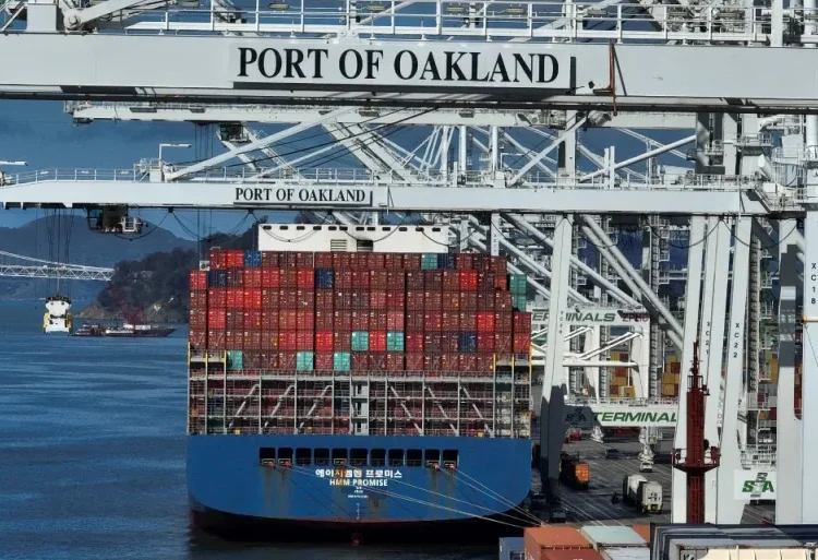 A shipping crane stands over a container ship at the Port of Oakland in Oakland, California