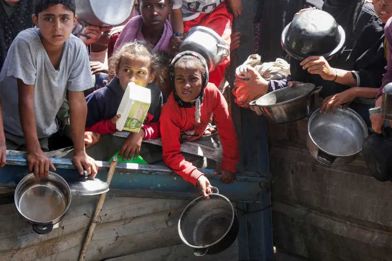 Palestinians wait to receive the food cooked by the charity kitchen as Israel's blockade results in Widespread hunger.