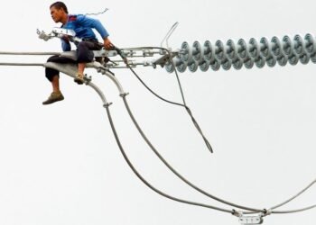 A worker in the Philippines installs a new electric cable atop a pylon.