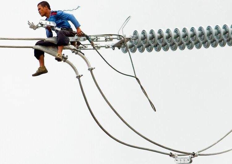 A worker in the Philippines installs a new electric cable atop a pylon.