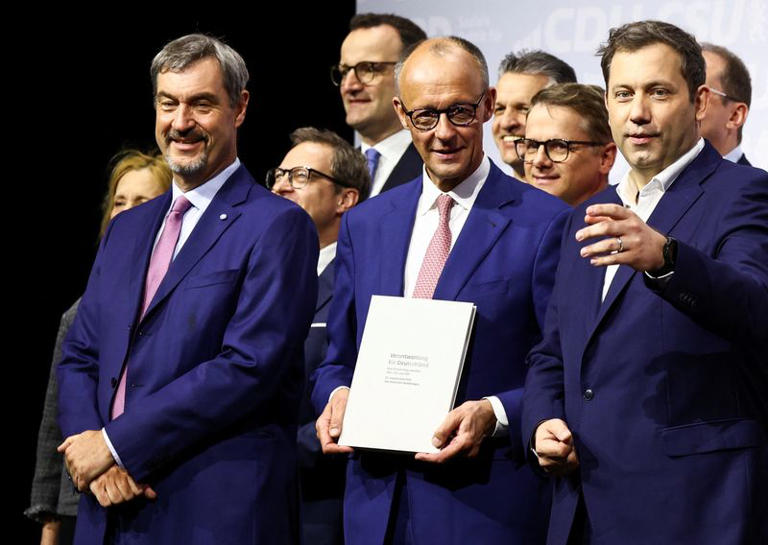 Germany’s Mainstream Parties Sign Coalition Deal 2 Incoming German Chancellor and leader of the Christian Democratic Union (CDU) Friedrich Merz holds the coalition government agreement between CDU, CSU and SPD, next to Christian Social Union (CSU) leader and Bavarian Premier Markus Soeder and Designated German Vice Chancellor and Designated Finance Minister Lars Klingbeil, at the Gasometer in Berlin, Germany May 5, 2025.