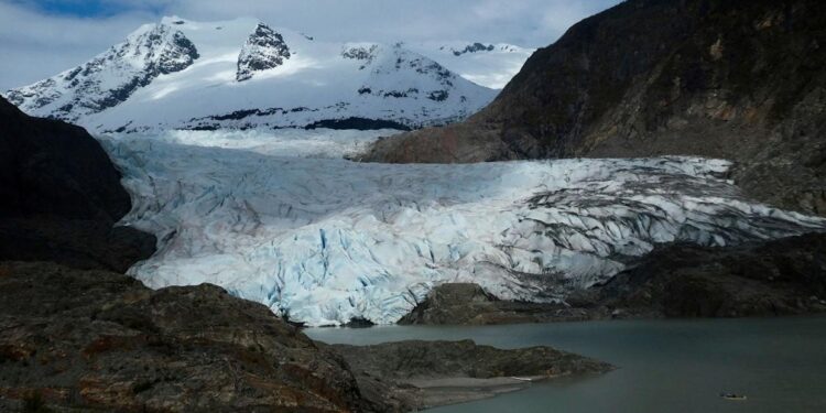 A canoe goes in front of a large glacier in Alaska.
