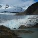 A canoe goes in front of a large glacier in Alaska.