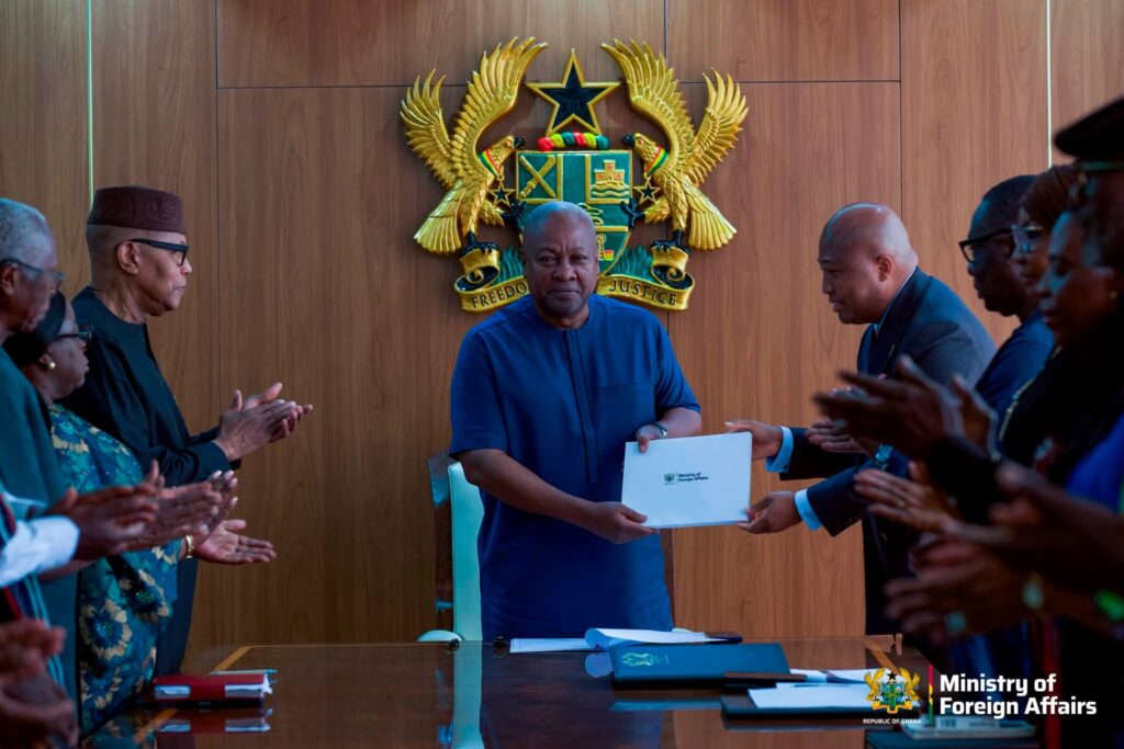 Foreign Affairs Minister Samuel Okudzeto Ablakwa presents the committee's report to President John Mahama at the Presidency in Accra, as committee members applaud.