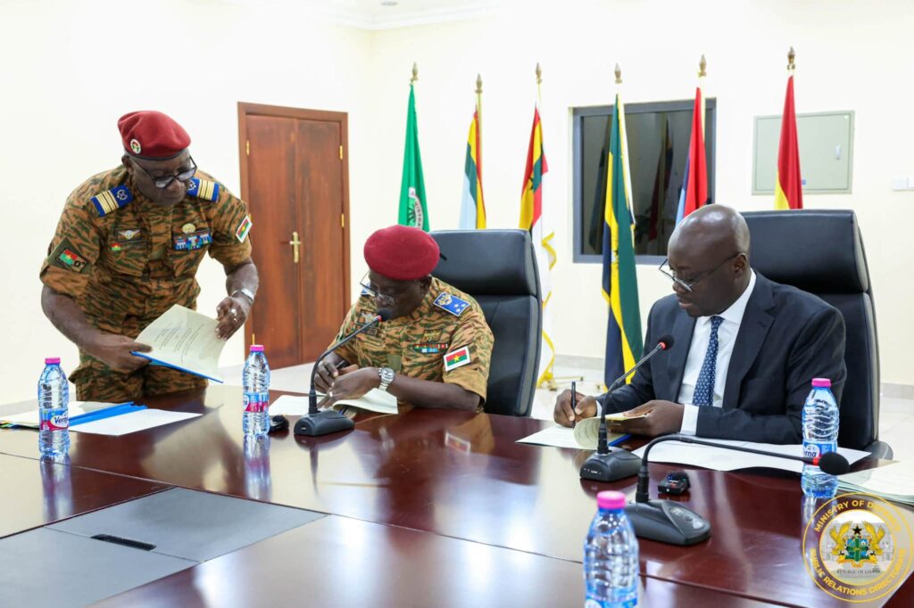Ghana, Burkina Faso Sign Defence Pact To Secure Trade Corridors 2 The two ministers append their signatures to the arrangement, assisted by a member of the Burkinabè delegation, as the documents are exchanged across the table. Photo: Ministry of Defence, Public Relations Directorate