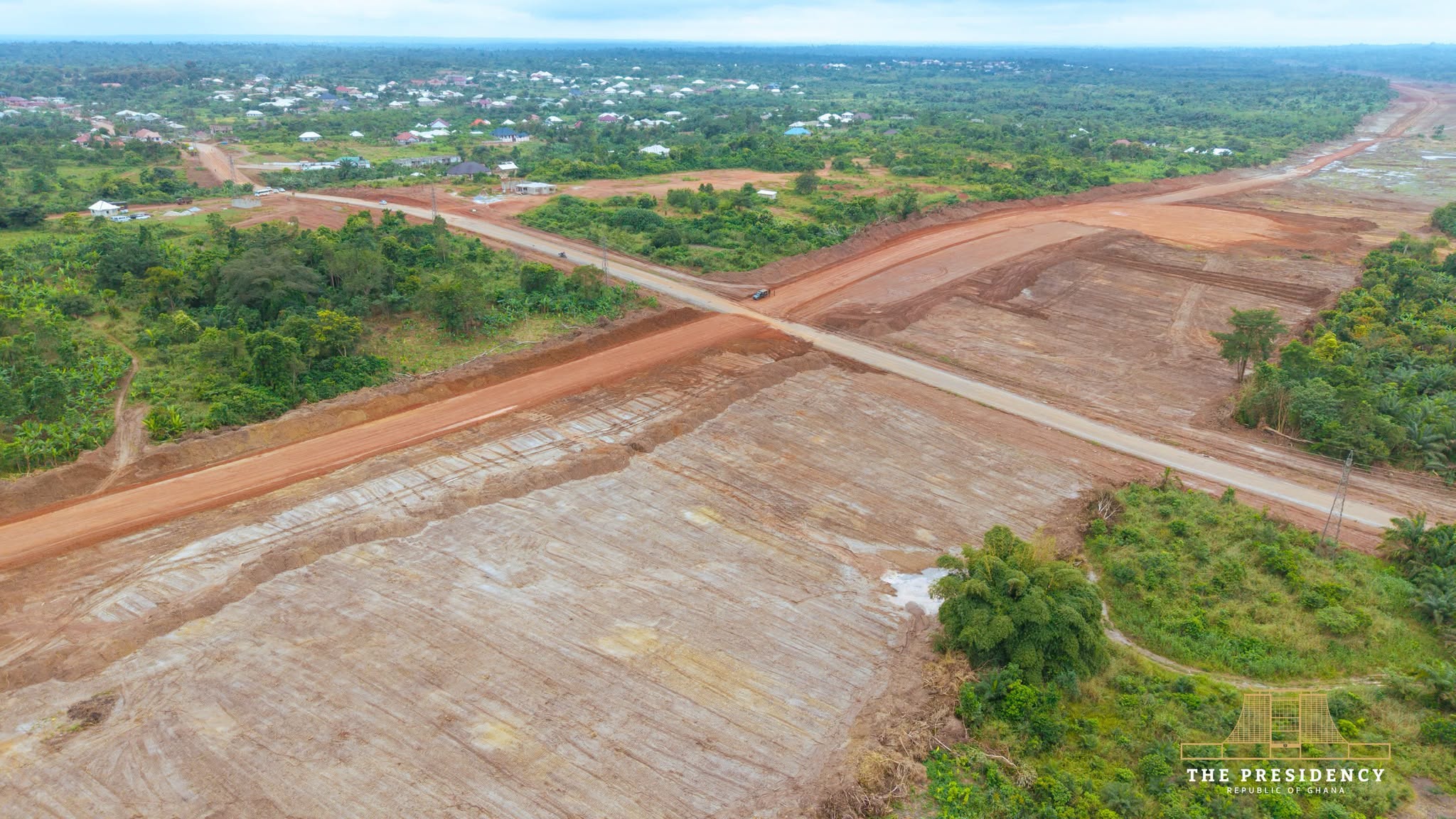 Aerial view of the cleared Accra-Kumasi Expressway corridor crossing an existing road beside a settlement