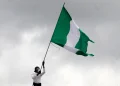 The green and white flag with the national coat of arms of Nigeria being waved during an outdoor gathering or protest