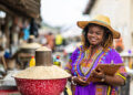 Portrait of Local African traditional woman entrepreneur, small business owner, SME, holding a clipboard at her outdoor market stall.