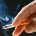 A hand holding a lit cigarette with a burning tip